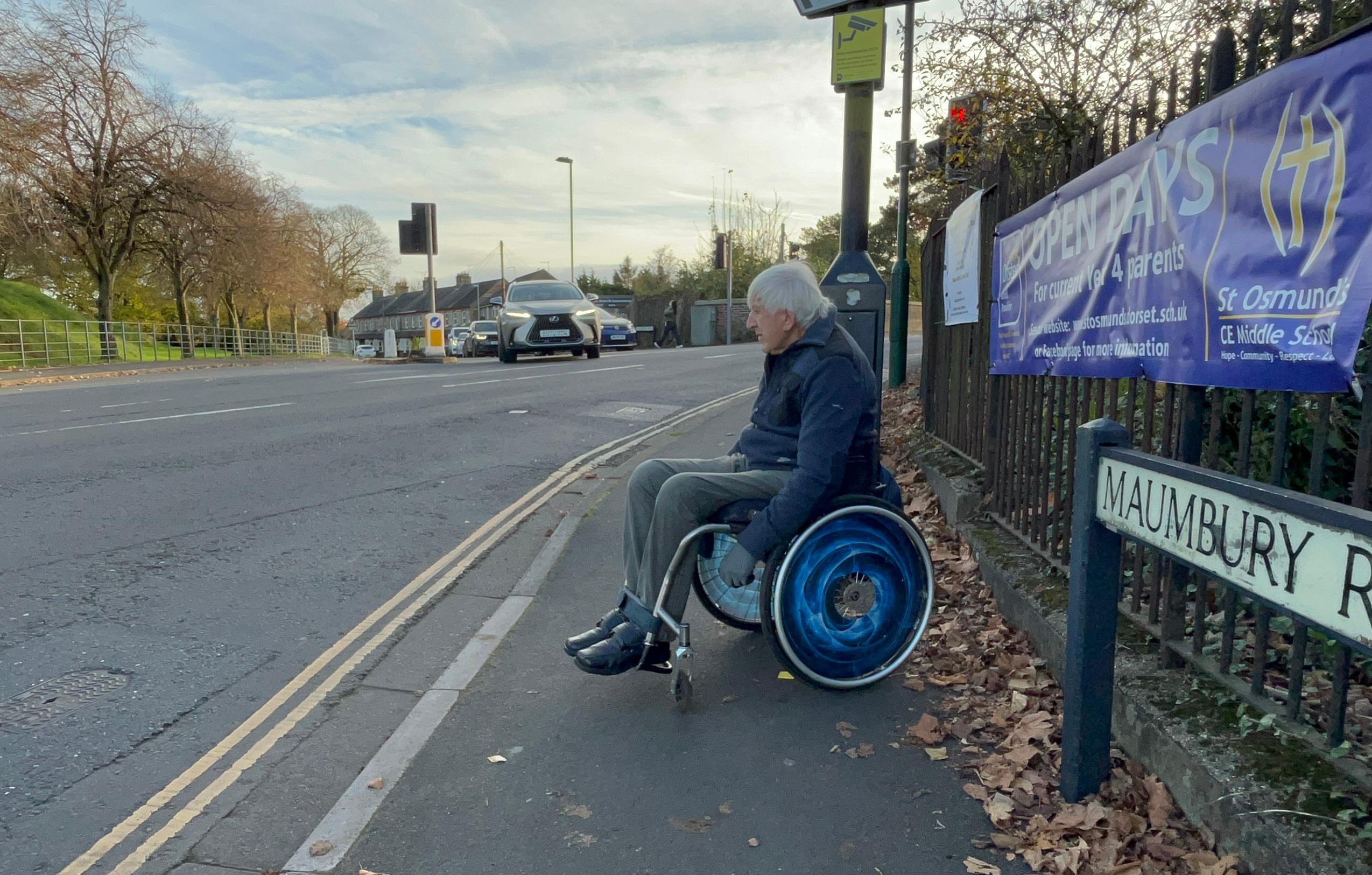 A man seated in a wheelchair waiting to cross a road